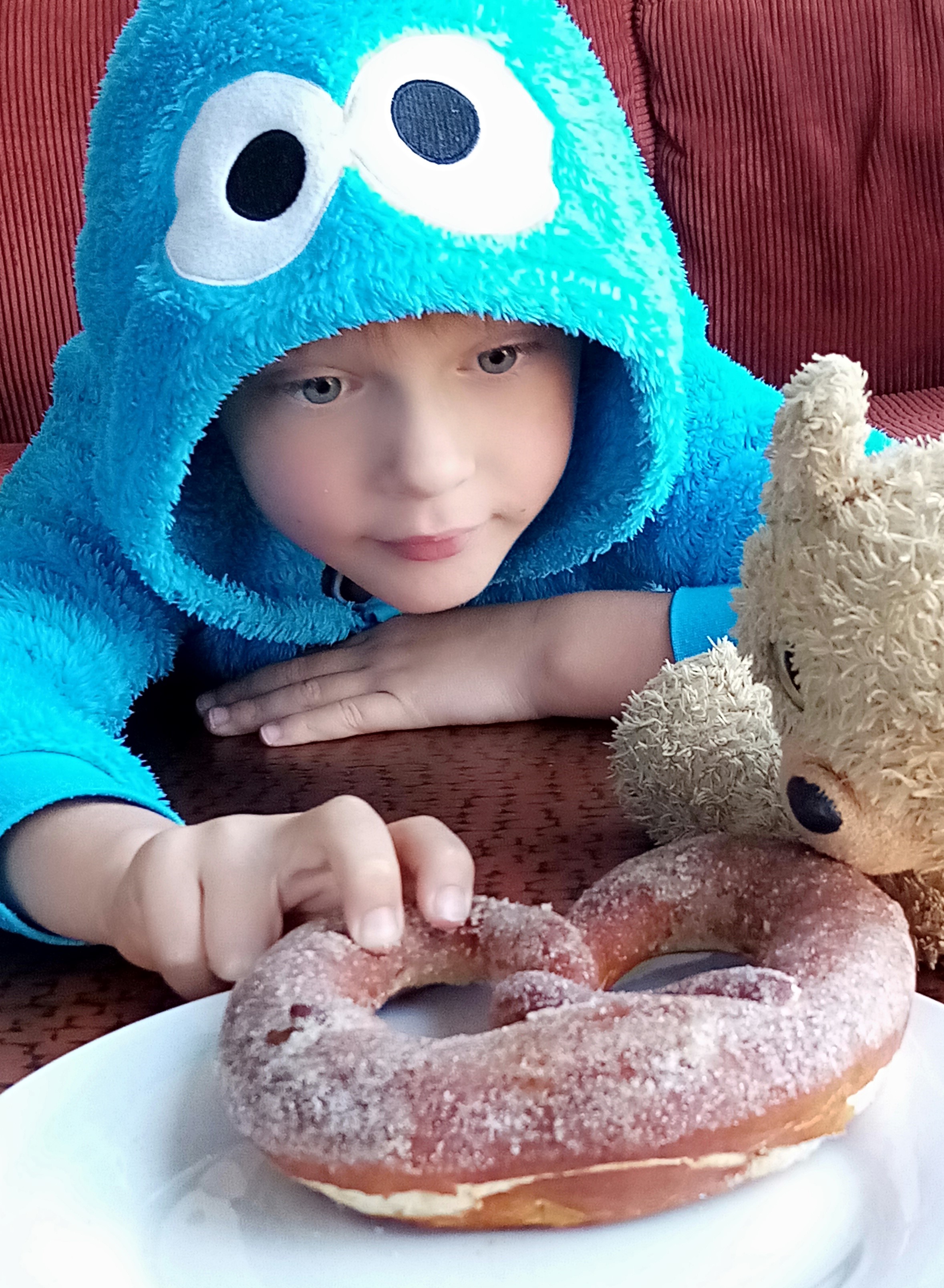 Picture of young boy reaching for a doughnout on a plate.