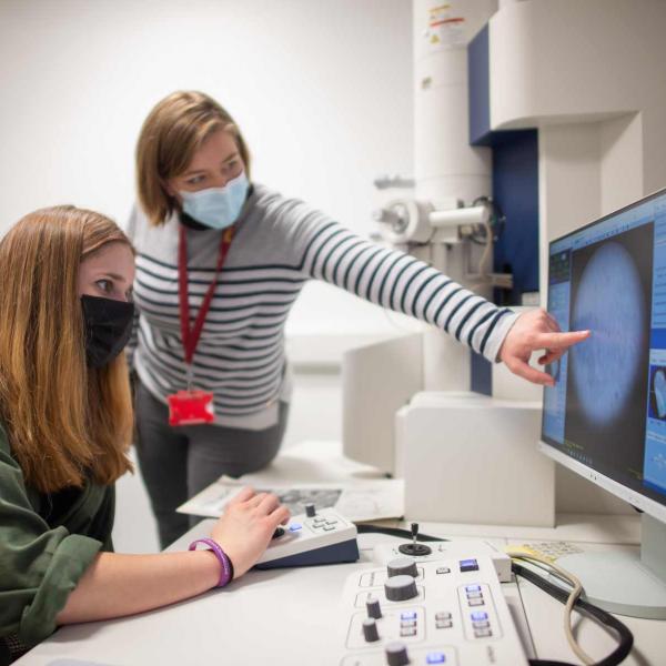 Dr. Natalie Doig points out features in the live camera feed from the transmission electron microscope as a school pupil navigates a specimen.