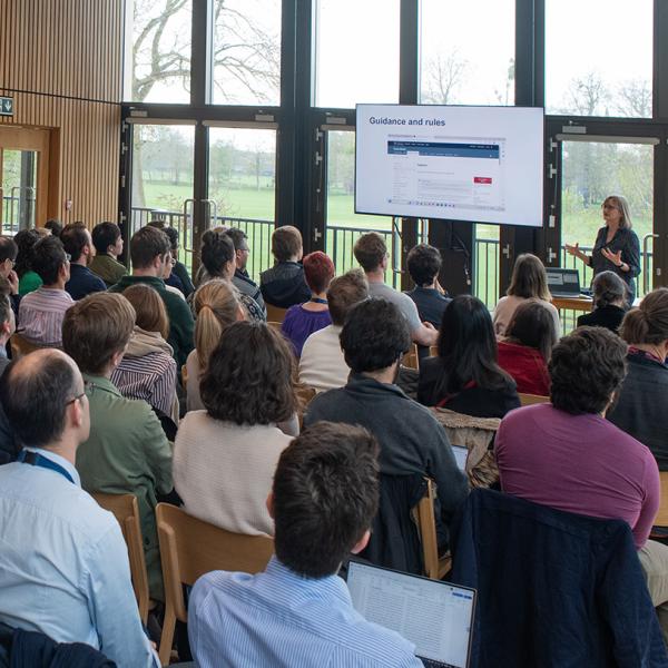 A room of people looking at a presentation screen. The room has a wall-to ceiling window behind the screen.