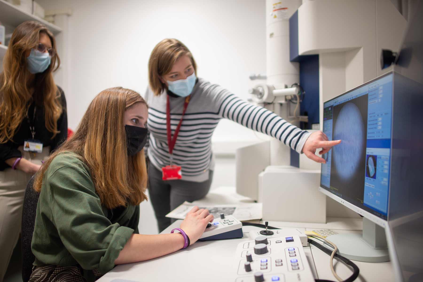 Dr. Natalie Doig points out features in the live camera feed from the transmission electron microscope as a school pupil navigates a specimen.