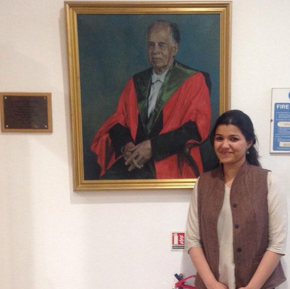 Unit student Abhilasha Joshi standing next to the department's portrait of Professor Sir William Paton.